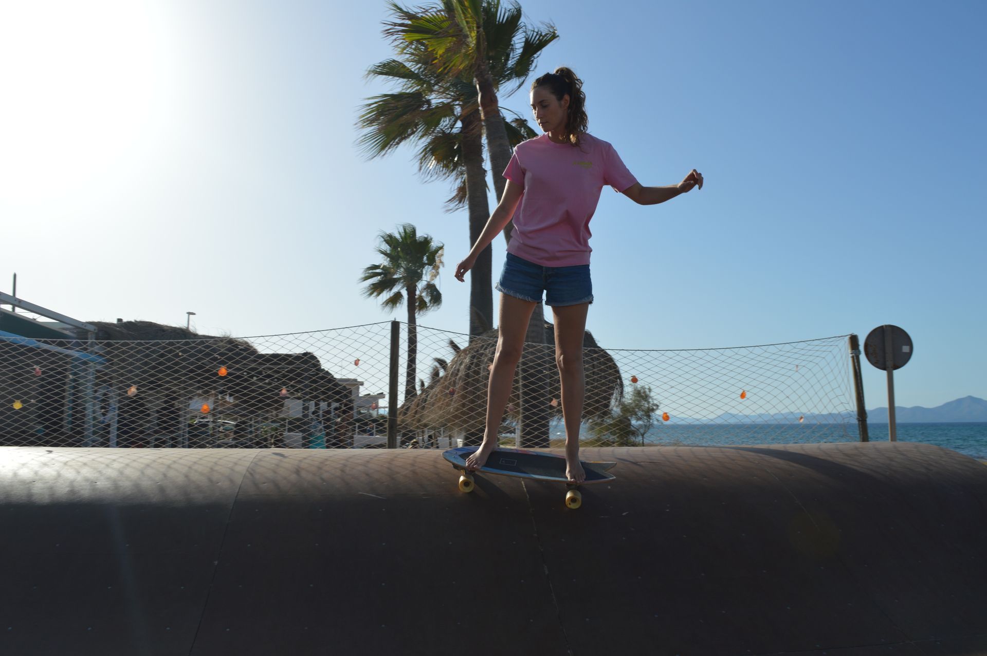 Una mujer con una camisa rosa está montando una patineta en una rampa.