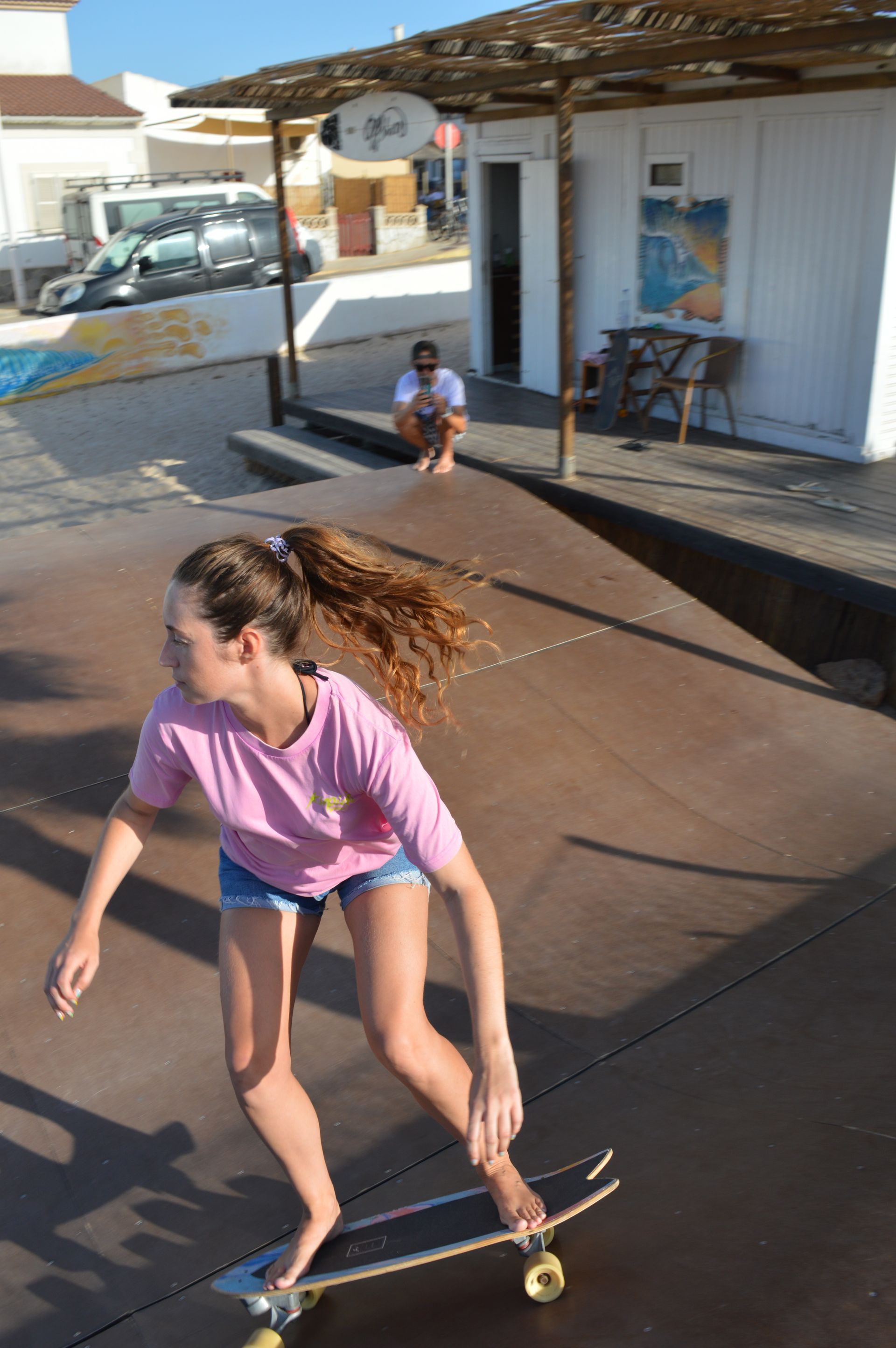 Una mujer con una camisa rosa está montando una patineta en una rampa.