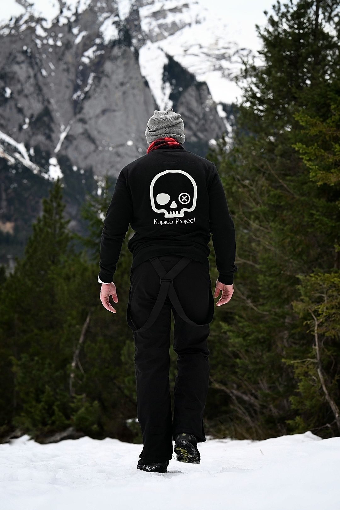 Un hombre que lleva una sudadera negra con una calavera en la espalda camina sobre la nieve.