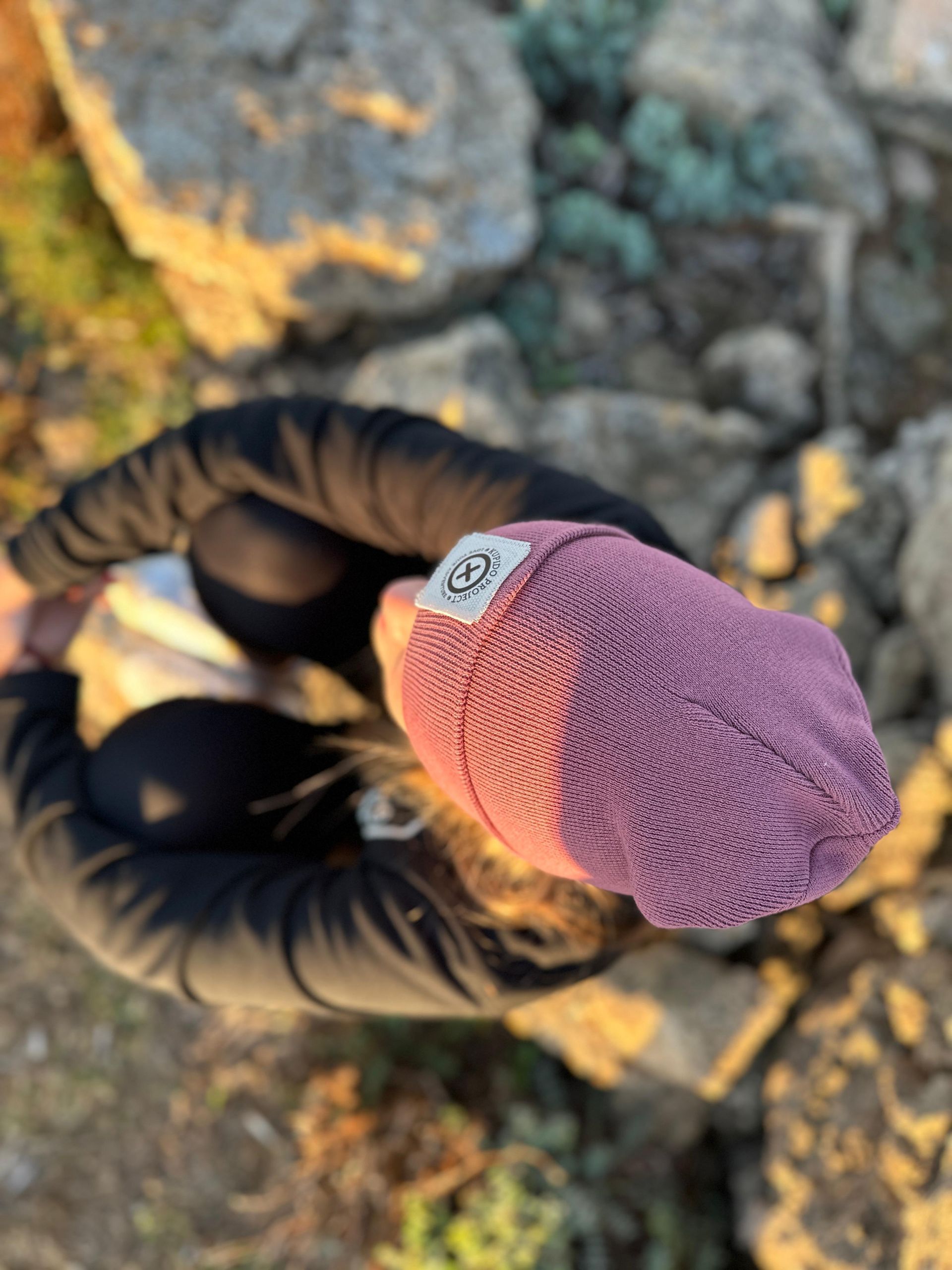 Una mujer que lleva un gorro morado está sentada sobre una roca.
