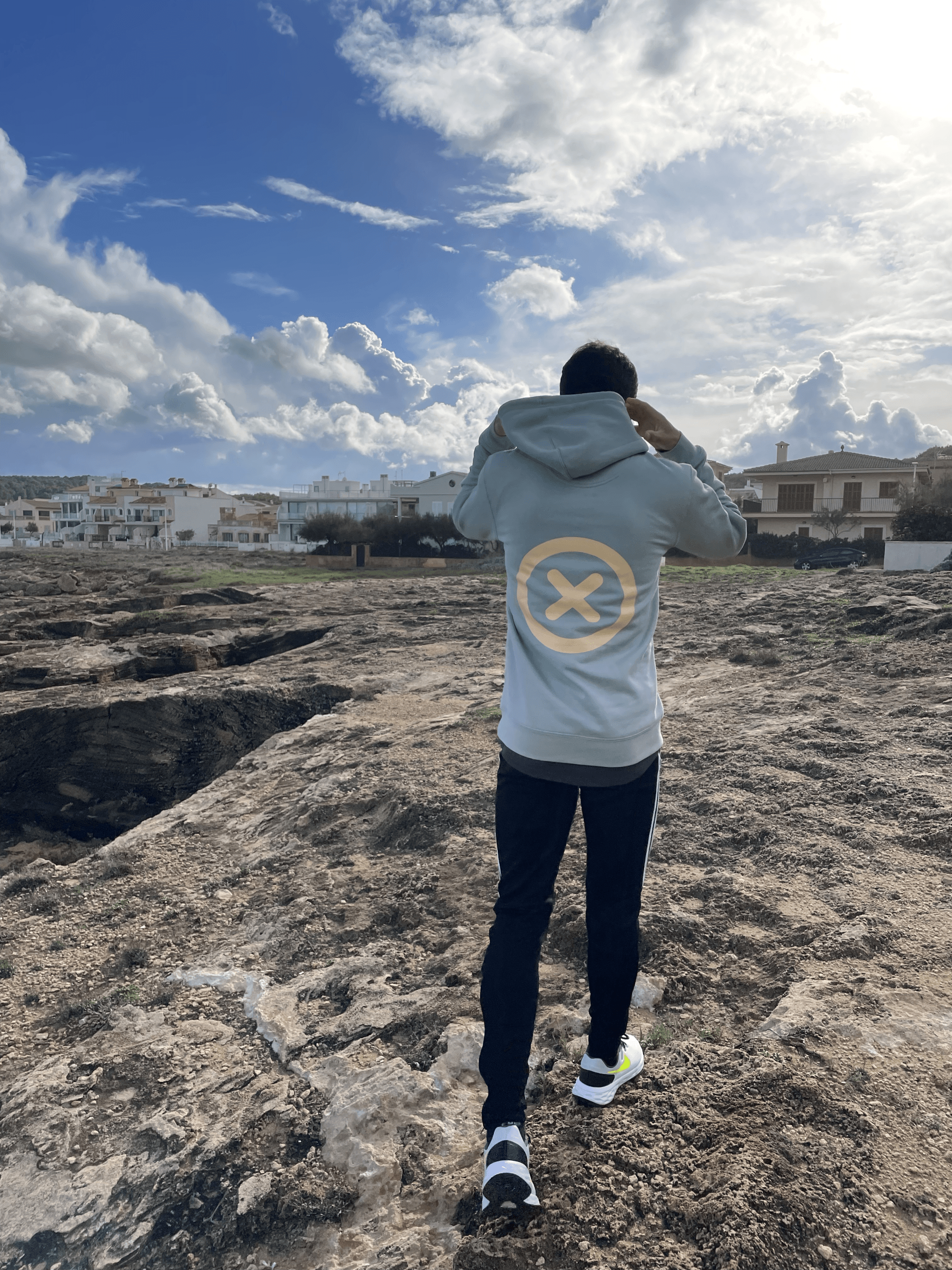 Un hombre con capucha está parado en la cima de una colina rocosa.