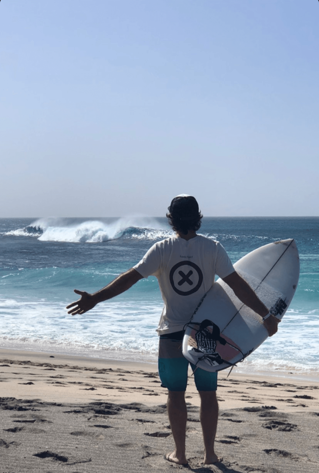 Un hombre está parado en una playa sosteniendo una tabla de surf.