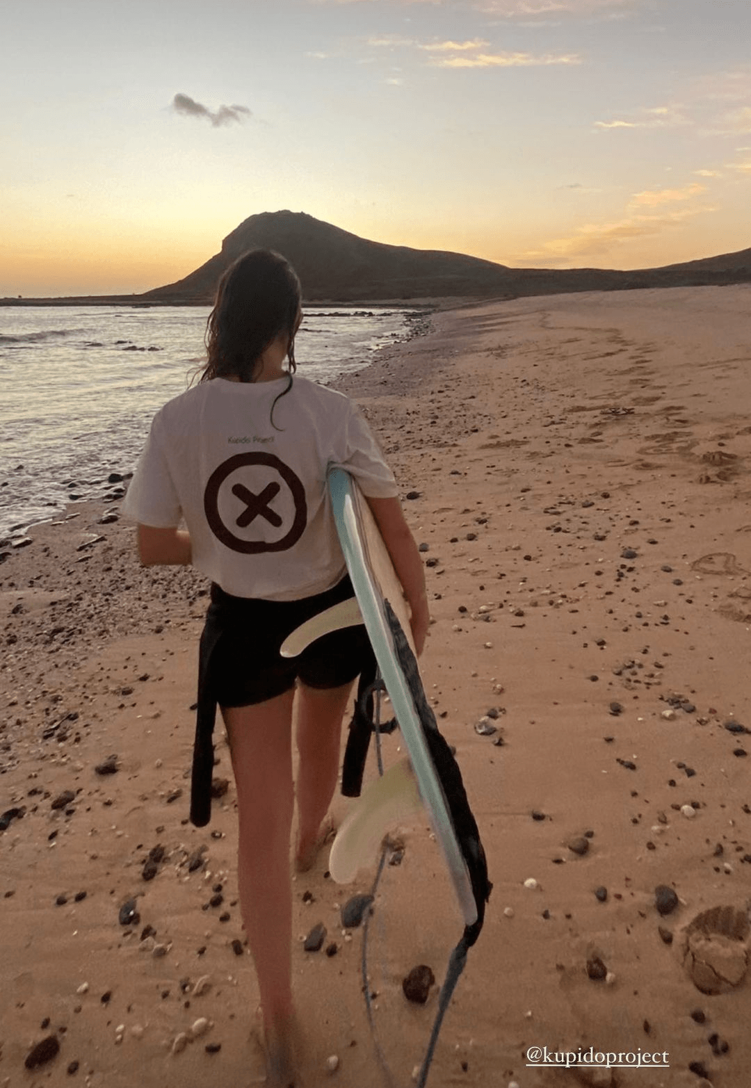 Una mujer camina por la playa cargando una tabla de surf.
