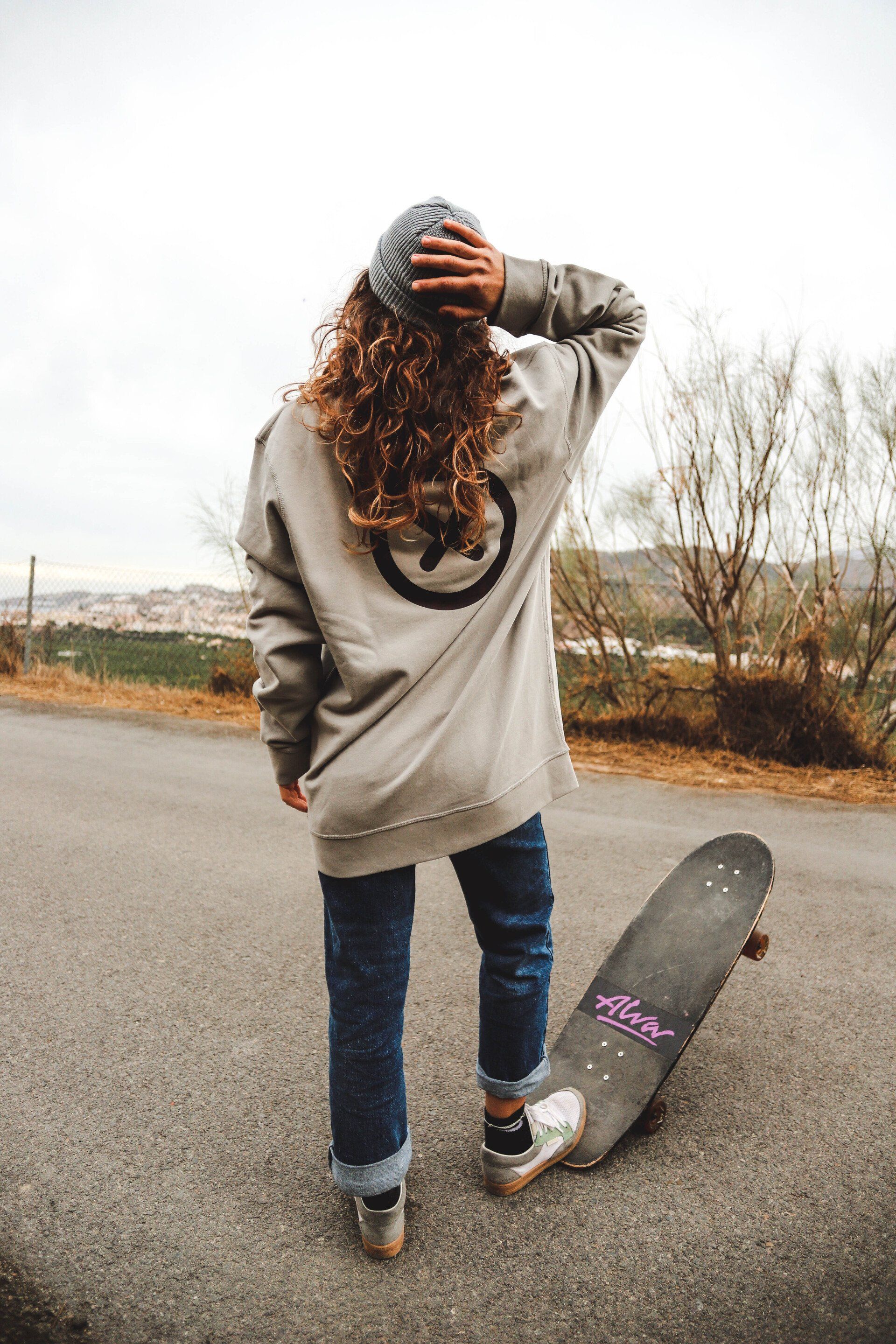 Una mujer está parada junto a un skateboard al costado de una carretera.