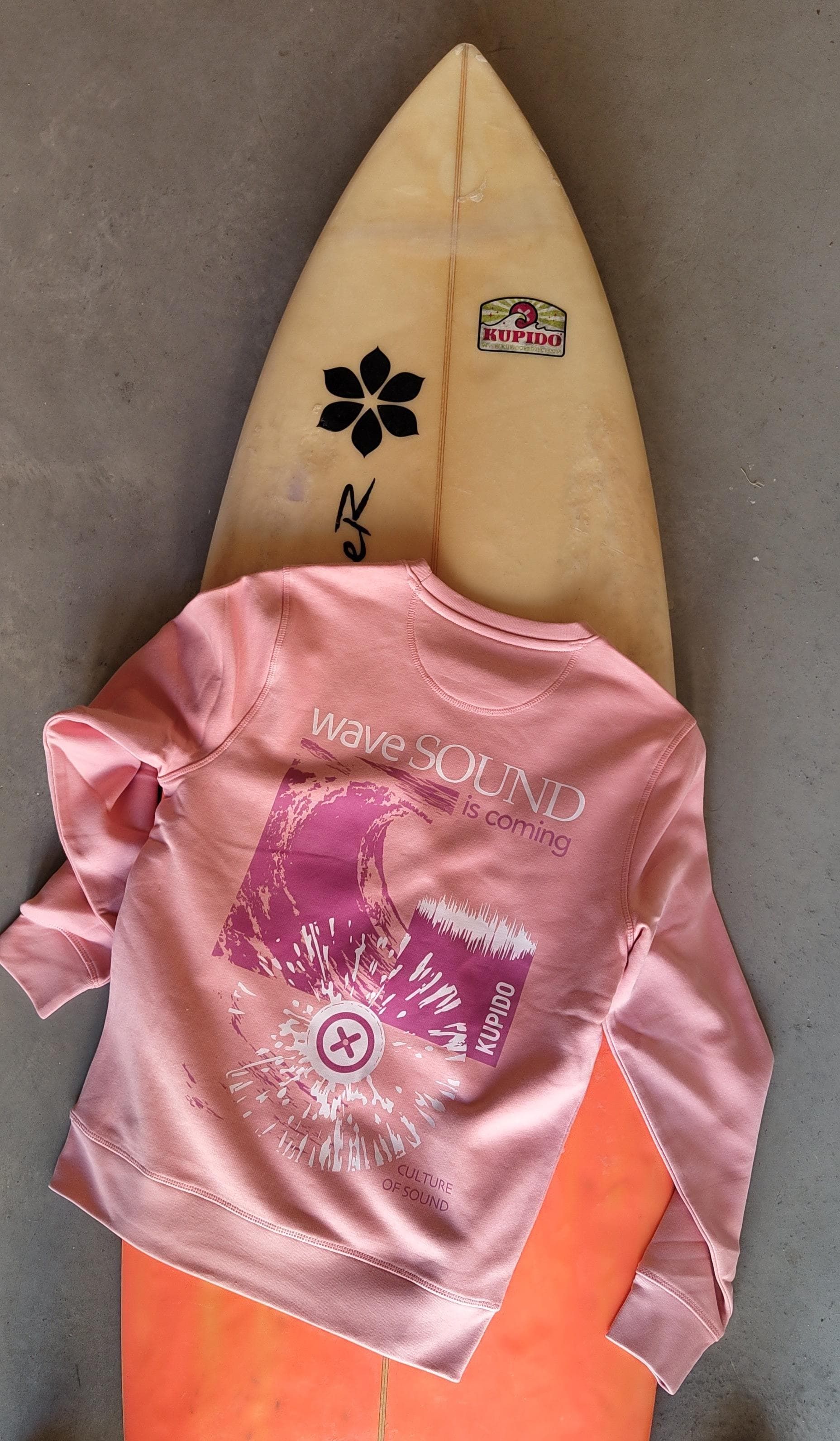 Una camisa rosa está encima de una tabla de surf naranja