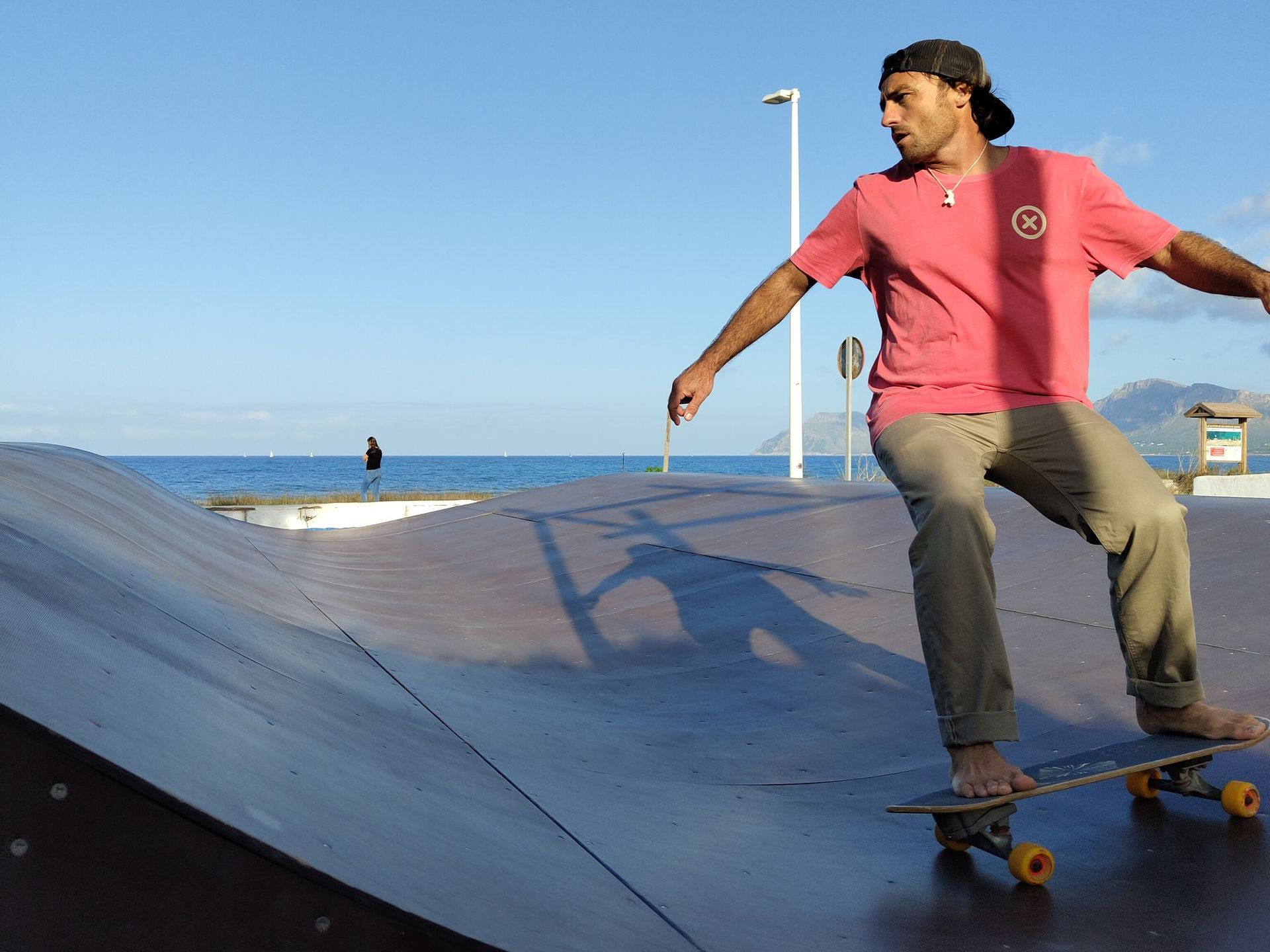 Un hombre con una camisa rosa anda en patineta.