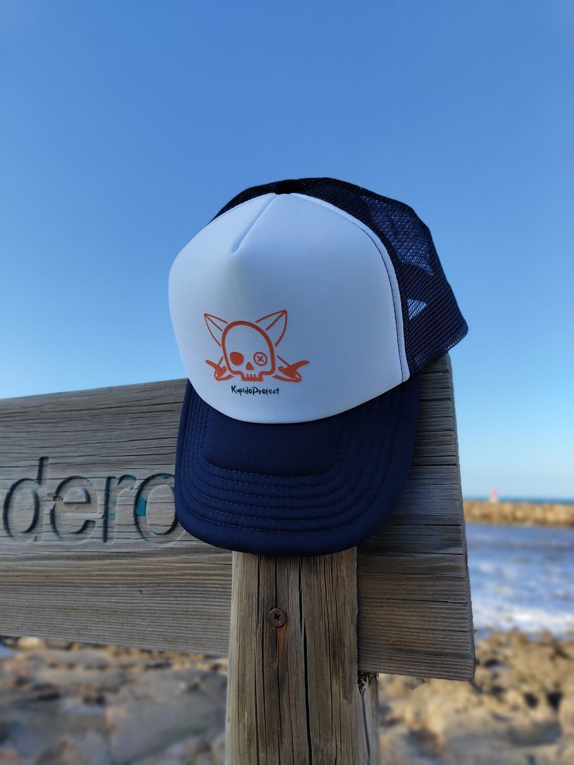 Una gorra trucker apoyada en un poste de madera cerca del océano