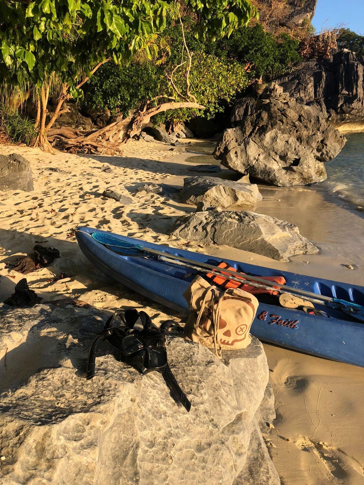 Un kayak azul está sentado encima de una roca en la playa.