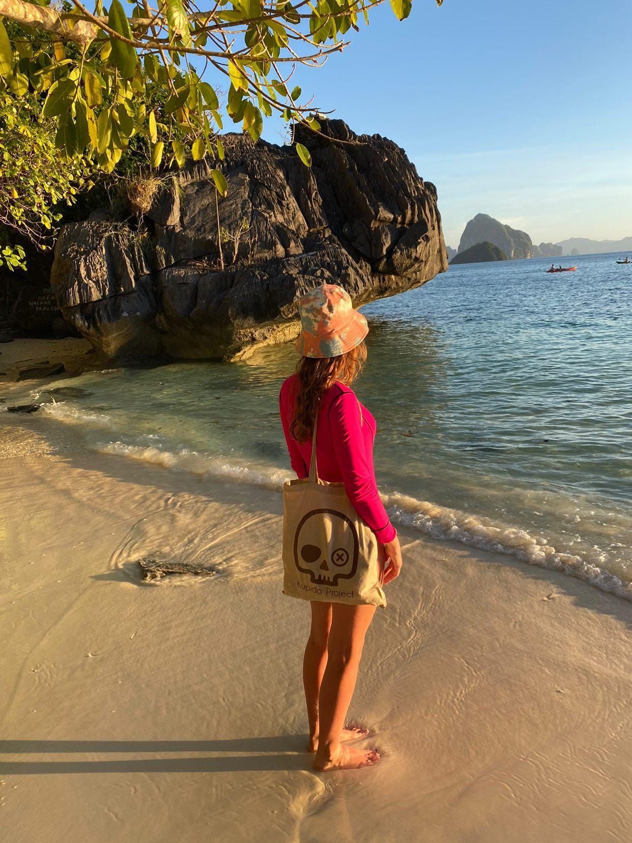 Una mujer está parada en una playa sosteniendo un bolso con una calavera.