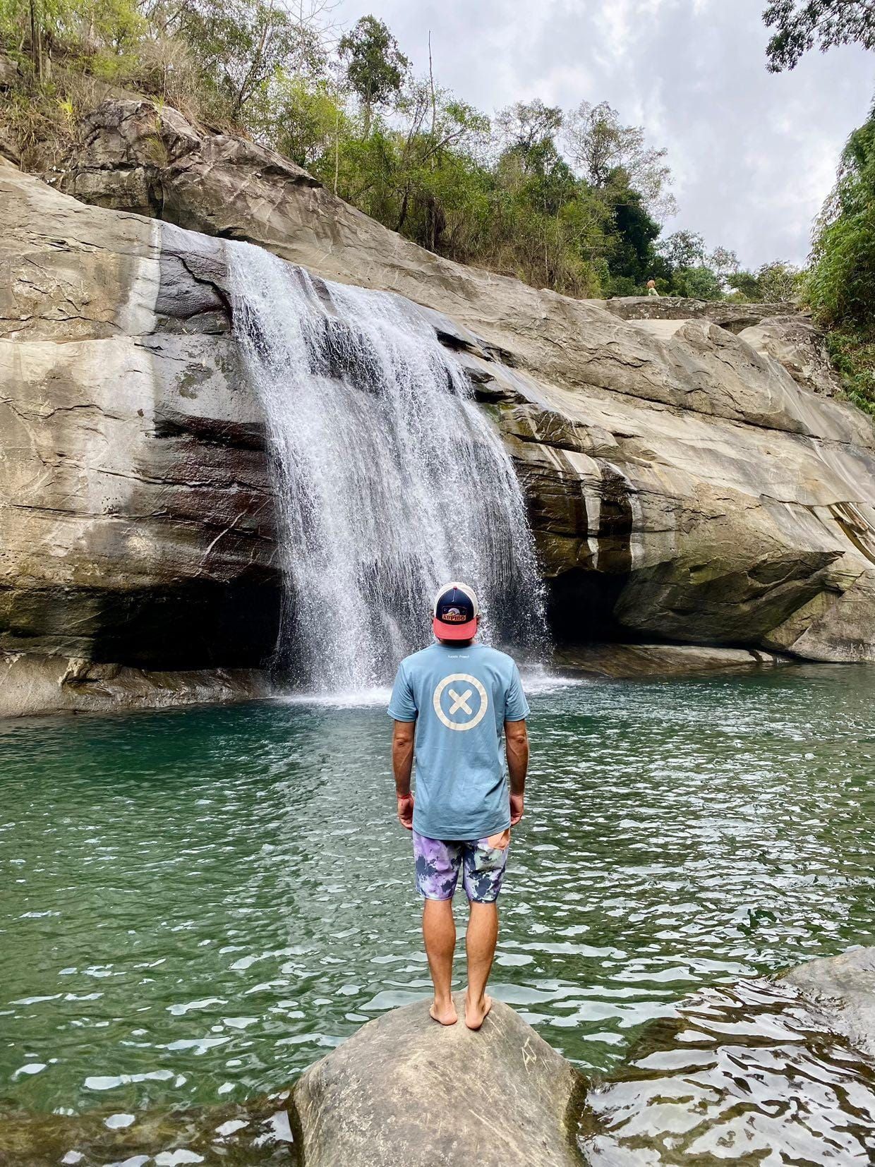 Un hombre está parado sobre una roca frente a una cascada.