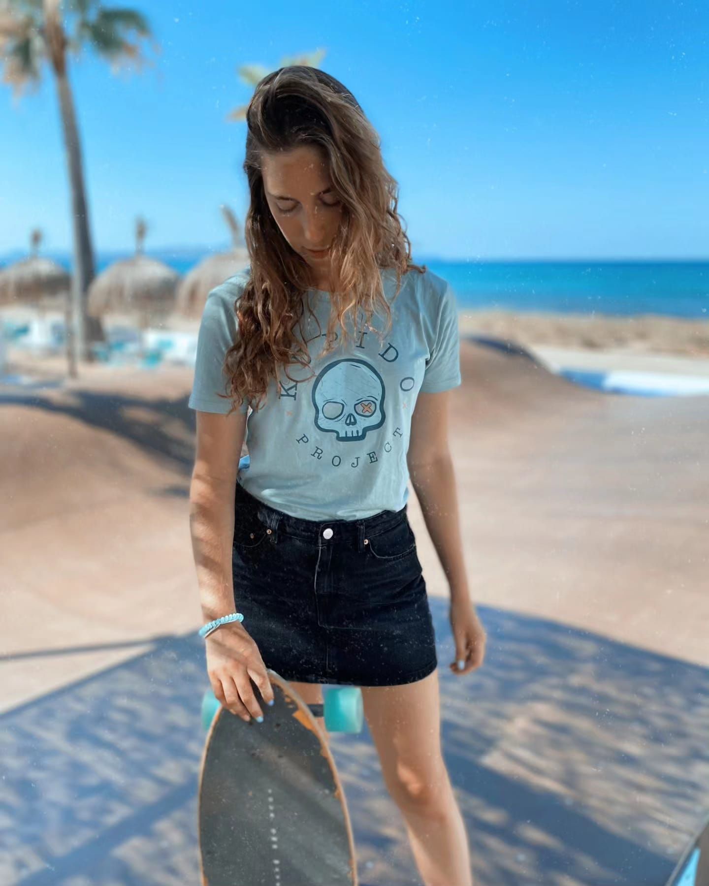 Una mujer está parada en una playa sosteniendo una patineta.