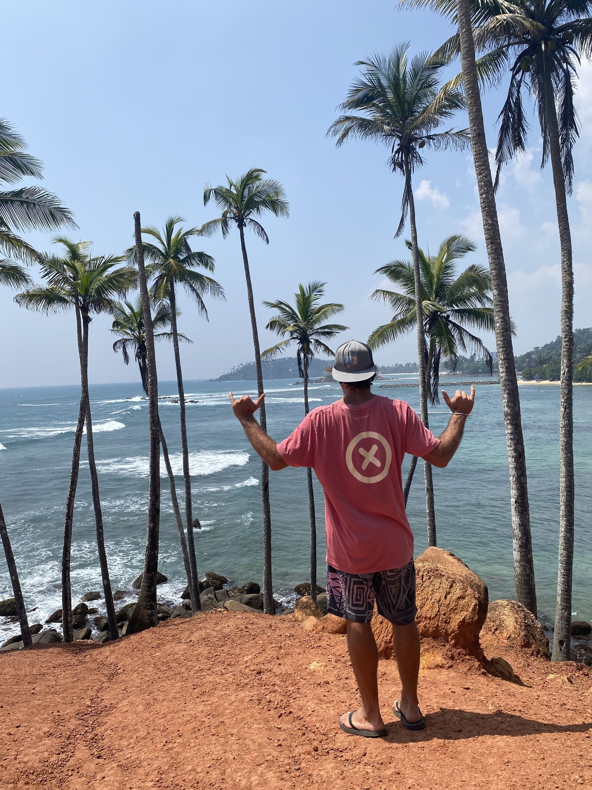 Un hombre con una camisa rosa y una x en la espalda está parado en la playa