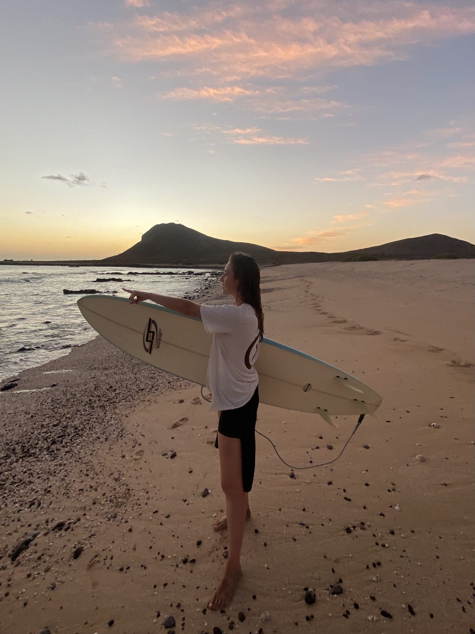 Una mujer sostiene una tabla de surf en la playa al atardecer