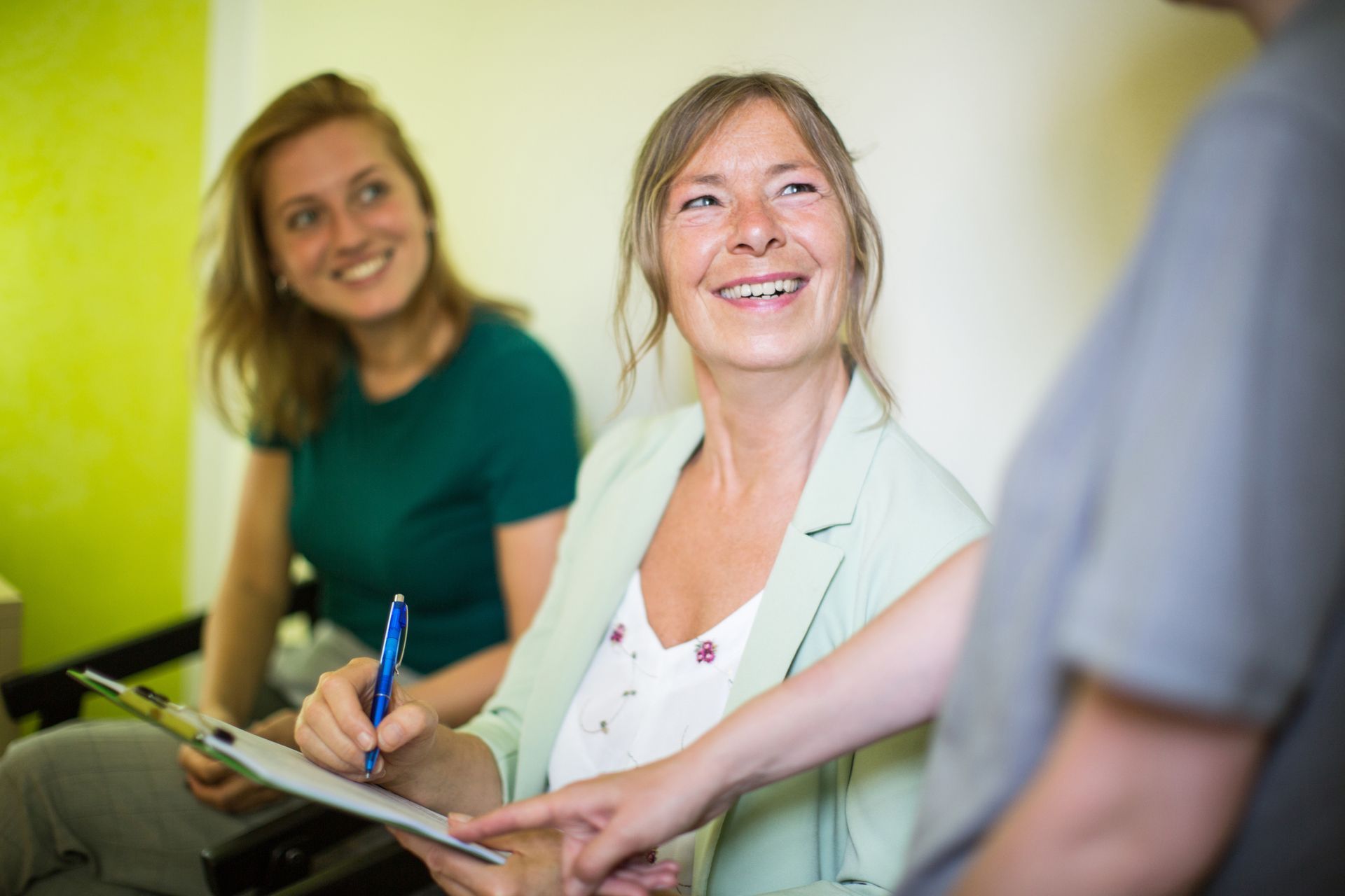 A woman is smiling while holding a clipboard in a waiting room.