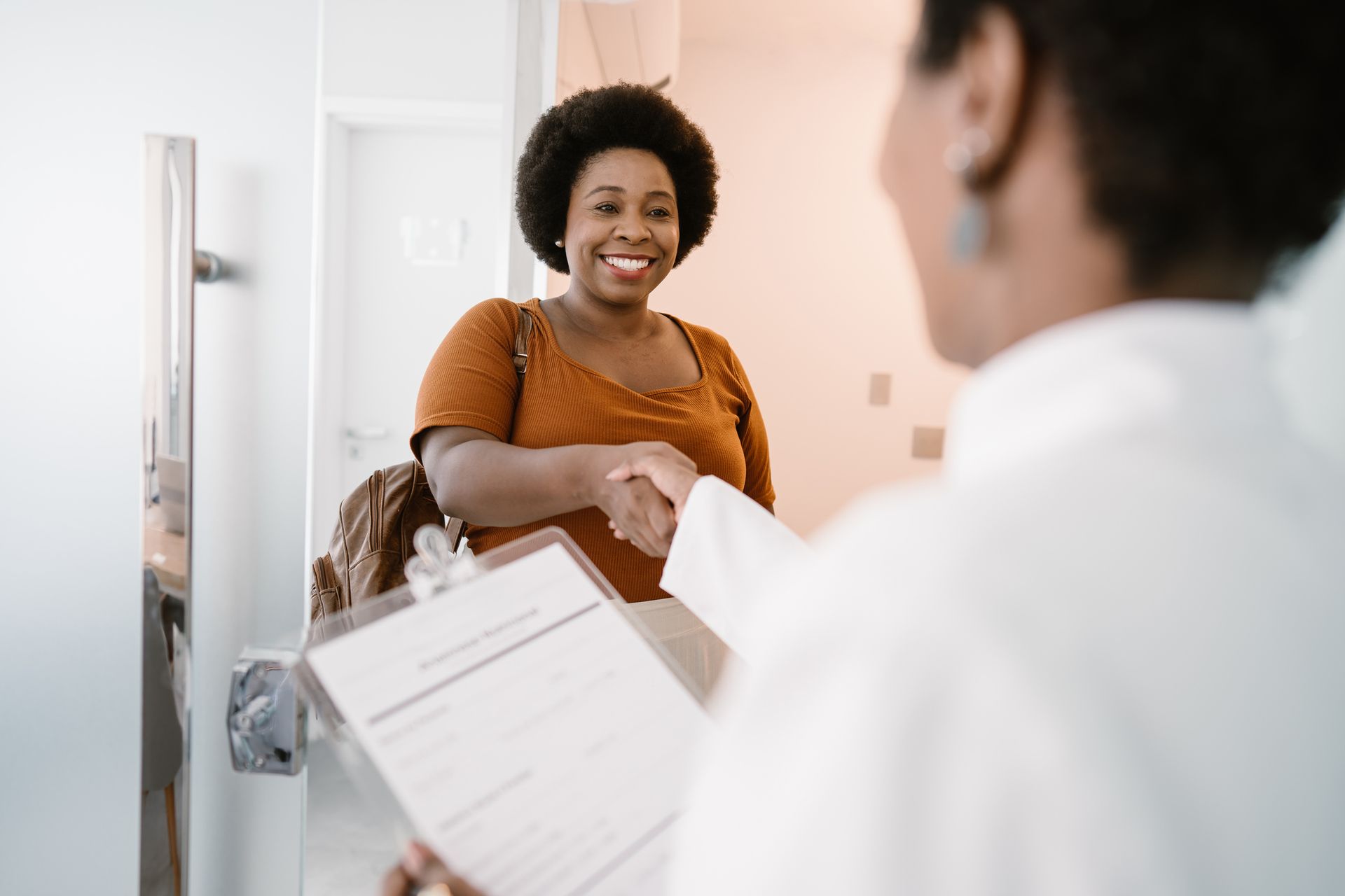 A woman is shaking hands with a doctor while holding a clipboard.