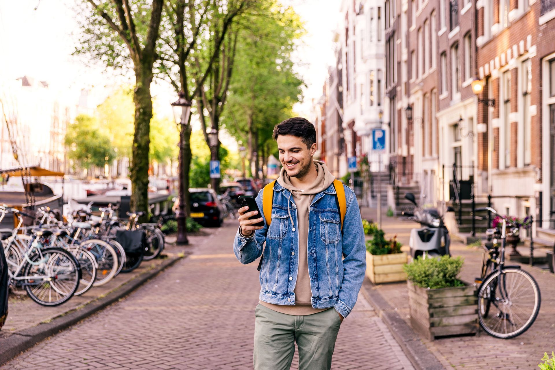 A man is walking down a street while looking at his cell phone.