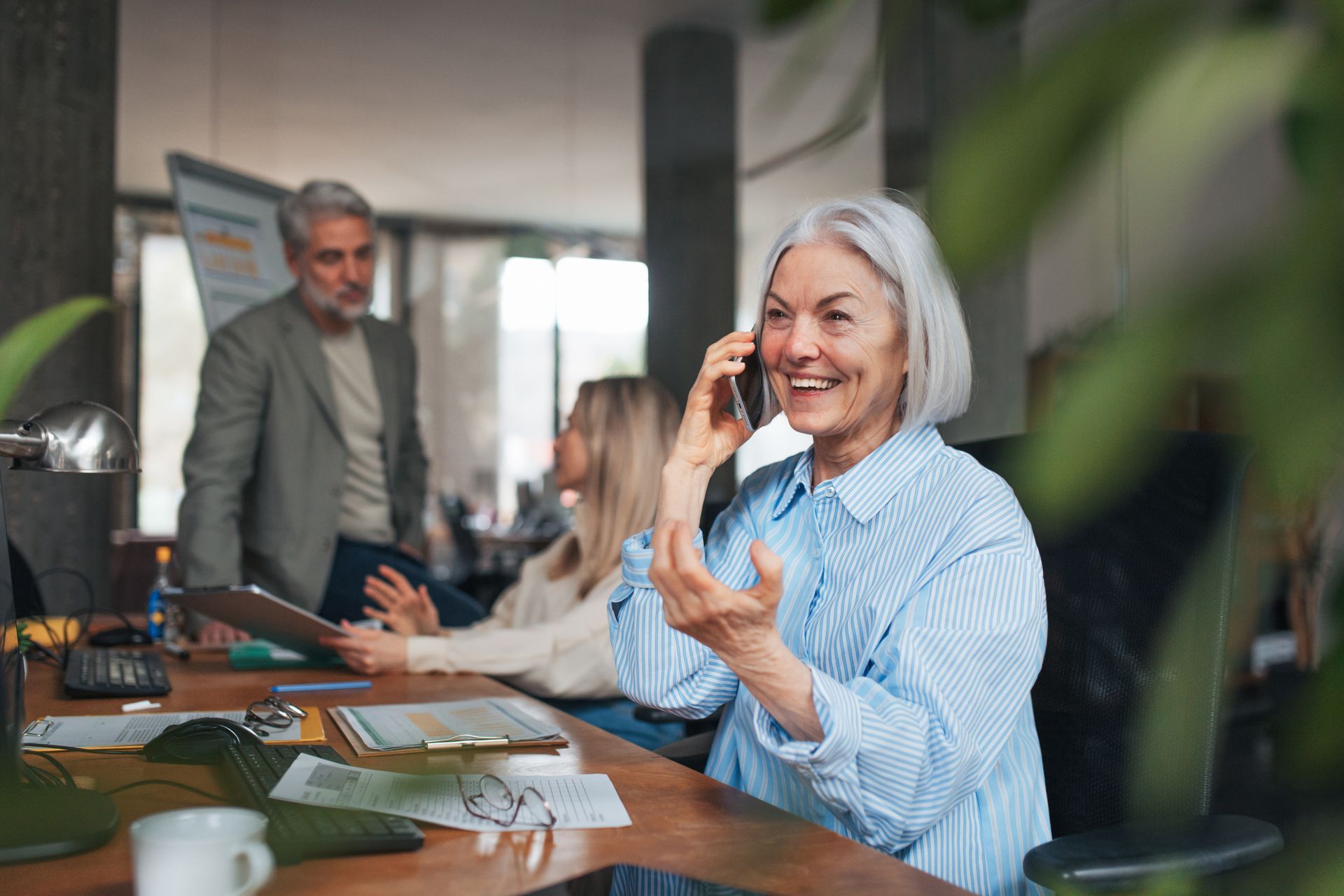 An elderly woman is sitting at a table talking on a cell phone.