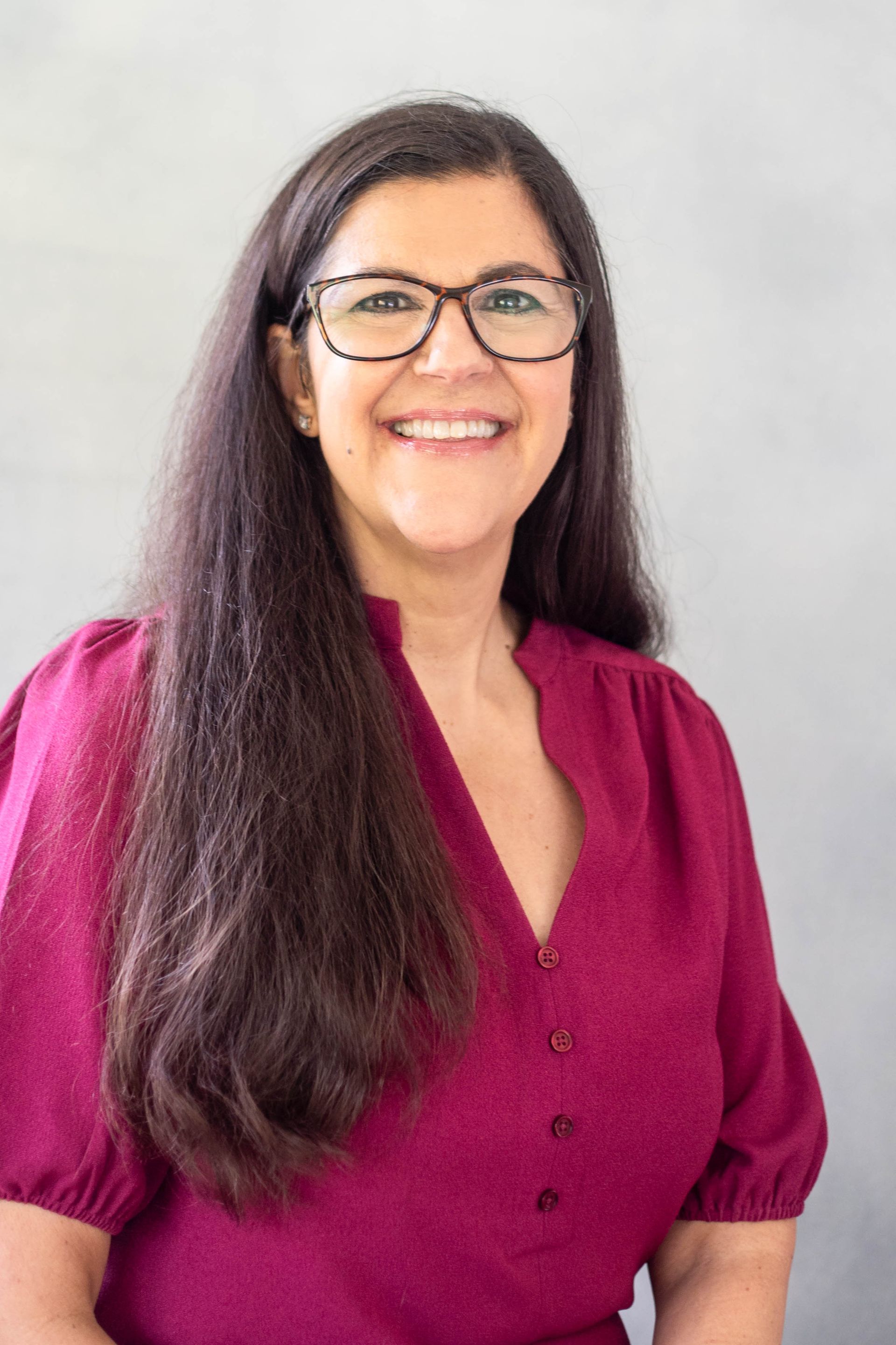 A woman wearing glasses and a red shirt is smiling for the camera.