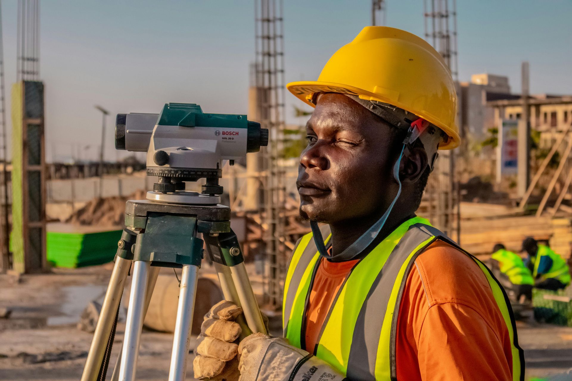 A construction worker is using a level on a tripod at a construction site.