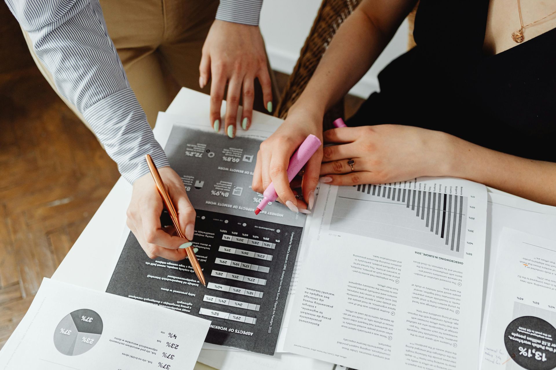 Two people reviewing business reports at a desk, highlighting data with a pen and highlighter.