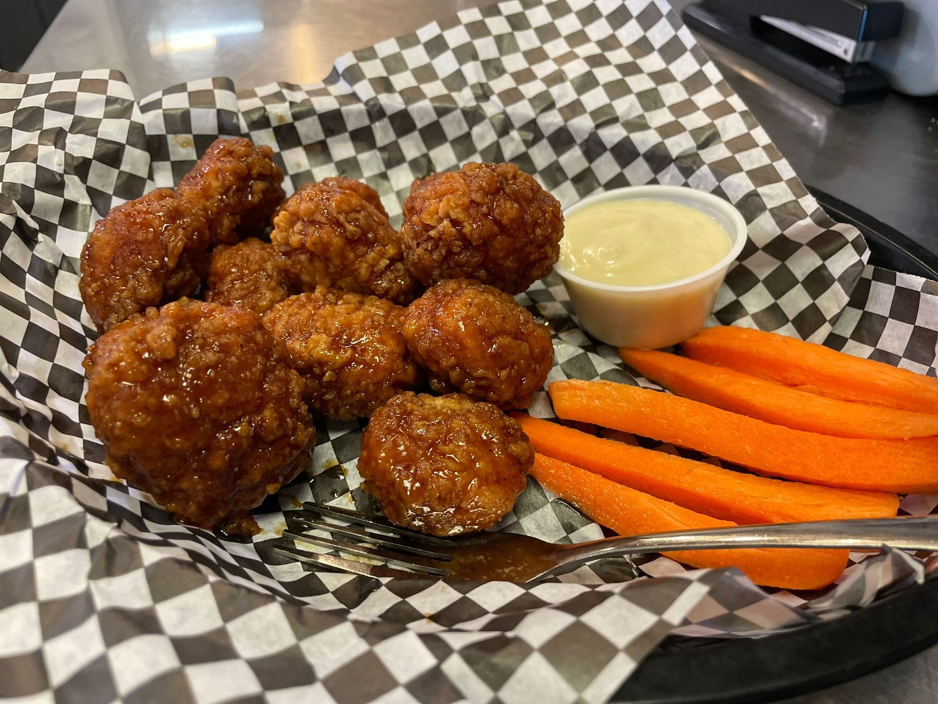 A basket of chicken nuggets and carrots with dipping sauce on a checkered paper.