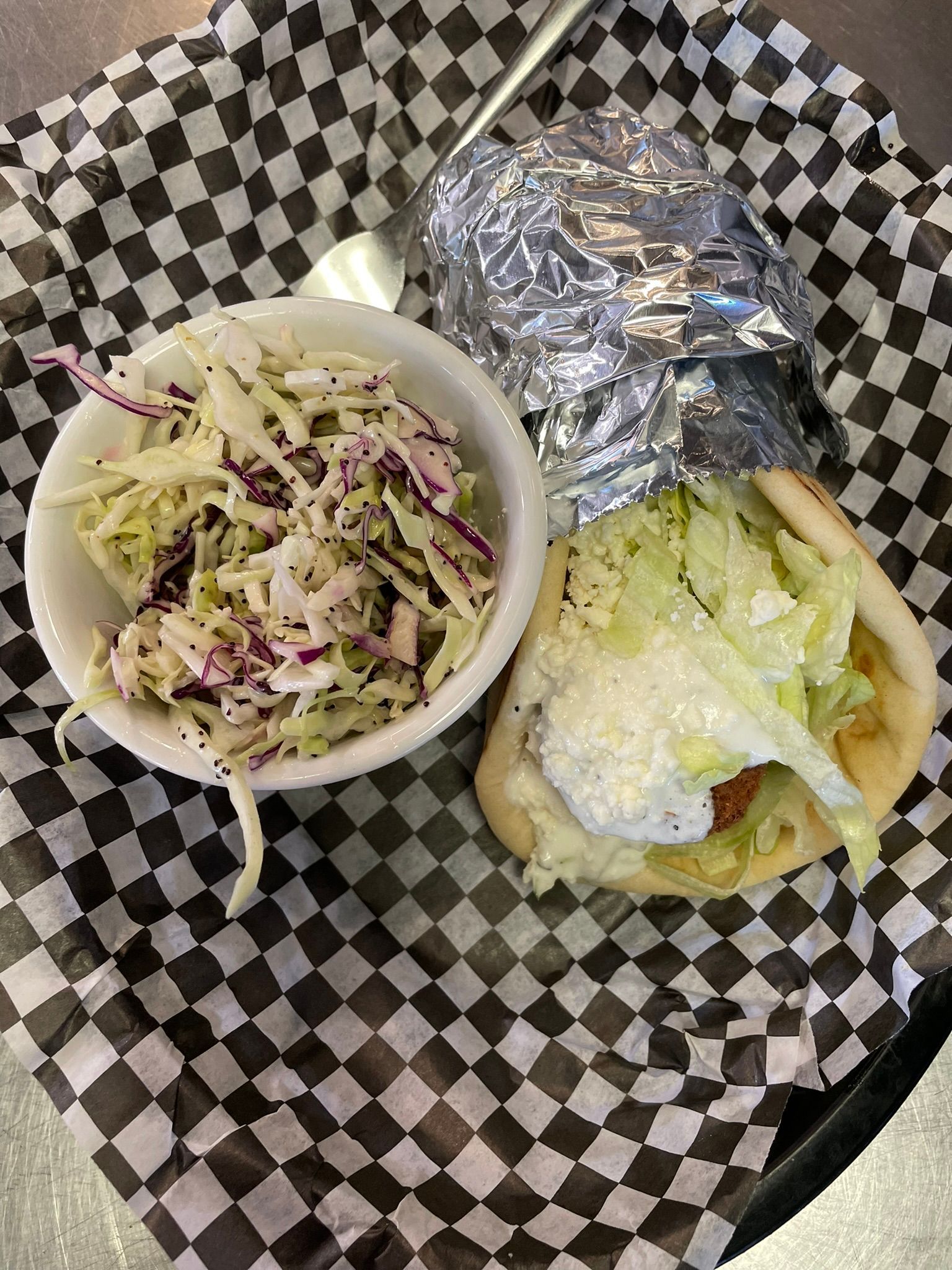 A sandwich and a bowl of coleslaw are on a checkered paper plate.