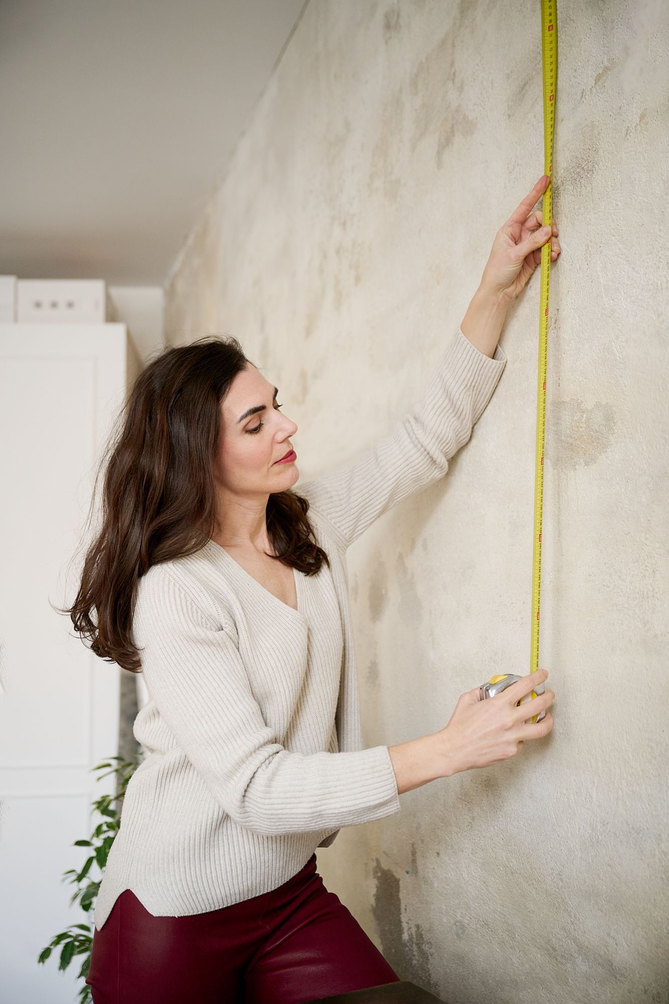 Une femme mesure un mur avec un mètre ruban dans un intérieur de maison