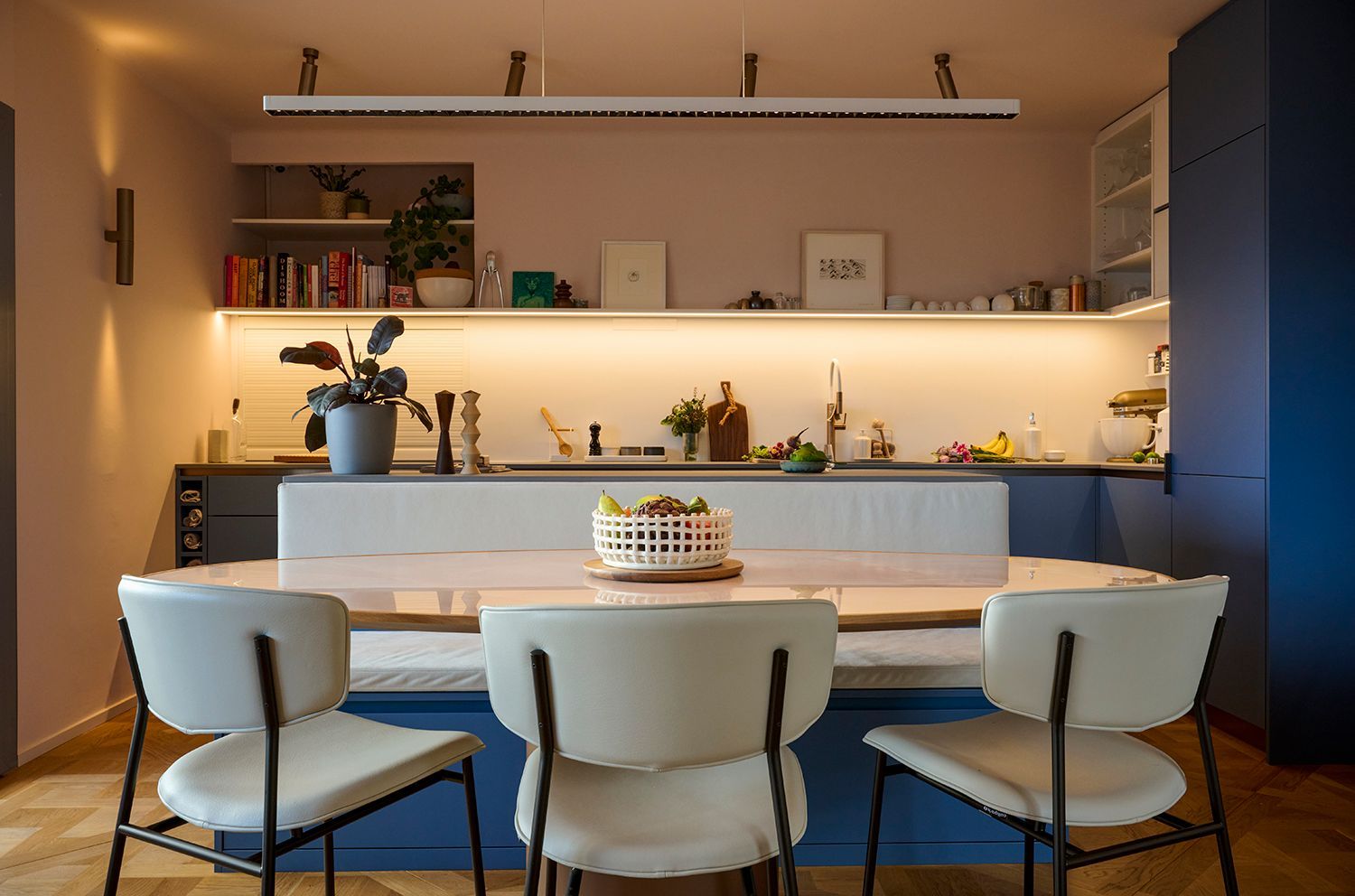 Salle à manger moderne avec table blanche, quatre chaises et étagères à éclairage chaleureux