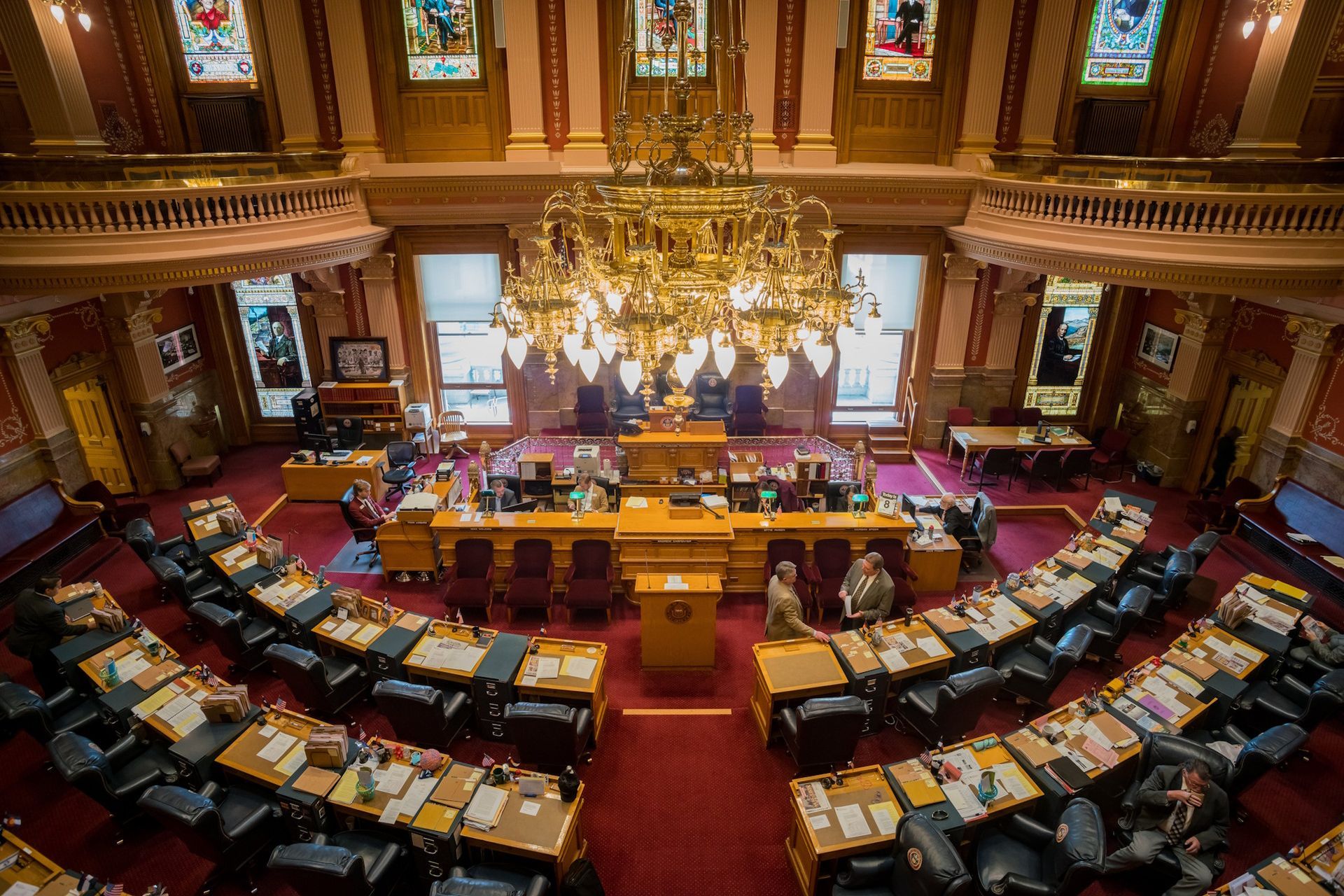 Legislative chamber with rows of desks and a chandelier. People are seated at the desks, possibly in a debate setting.