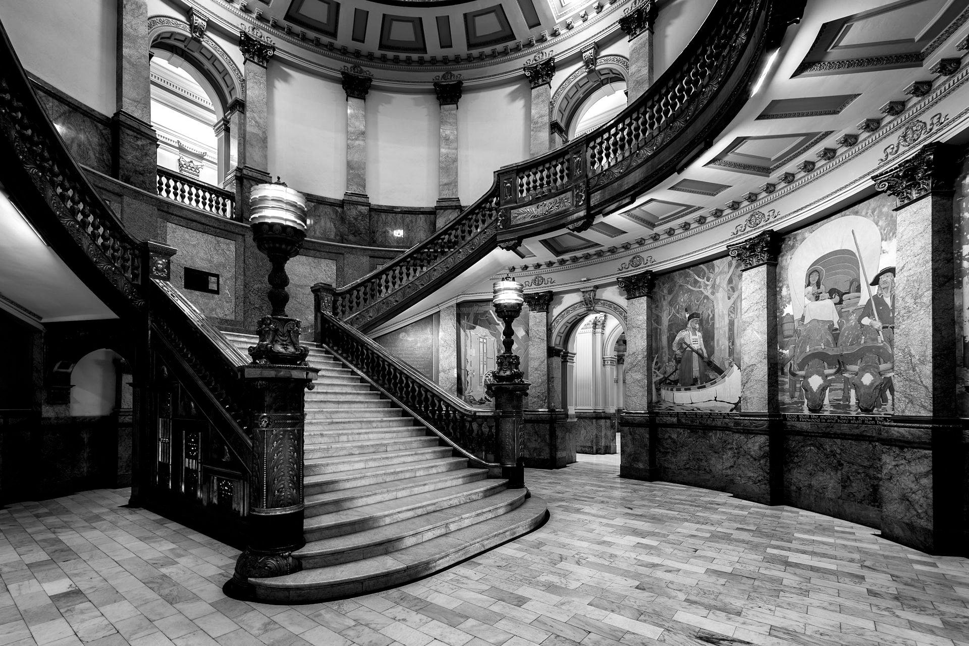 Elegant staircase in ornate hall with curved railings and decorative murals.
