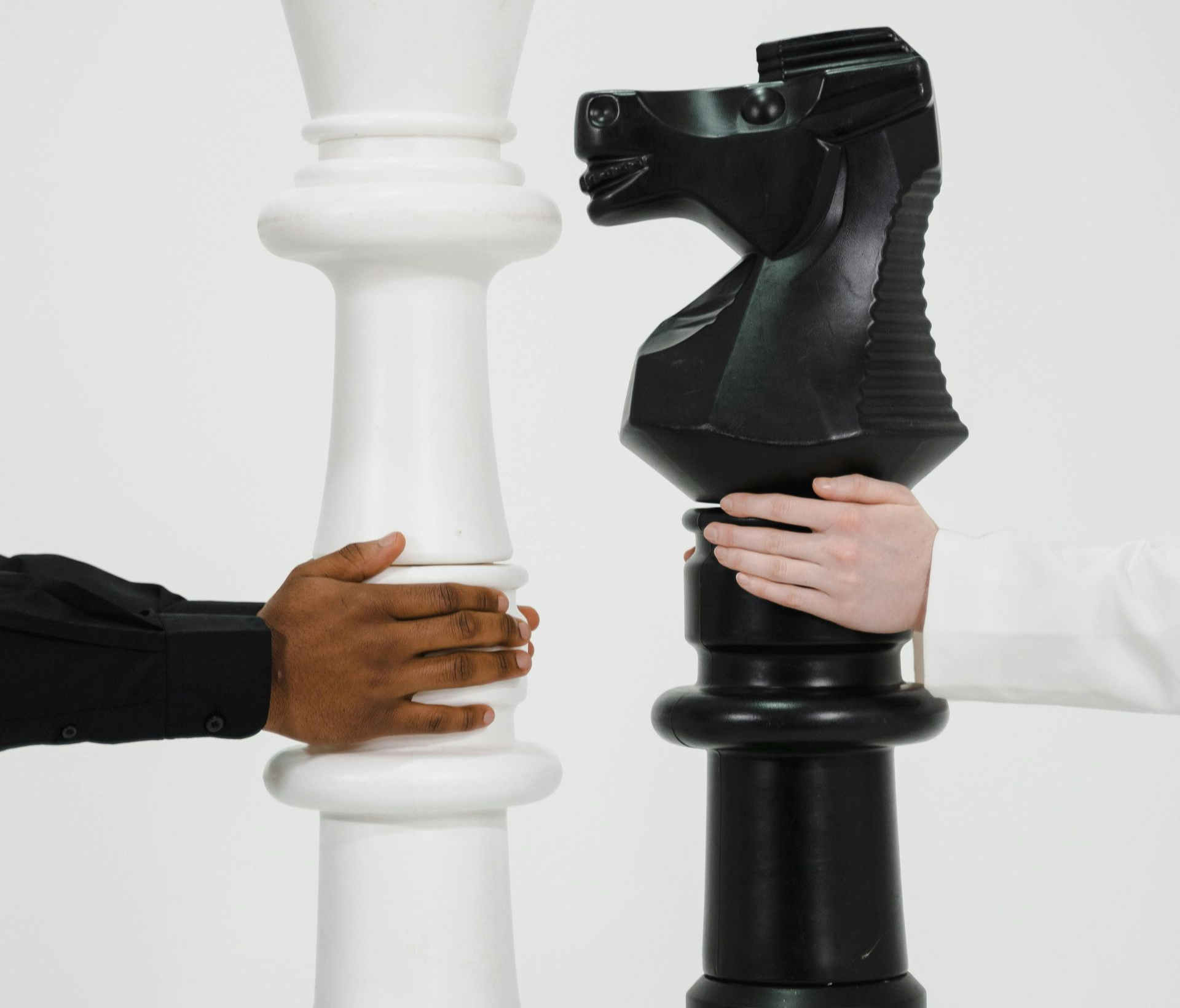Hands holding giant chess pieces: white queen, black knight.