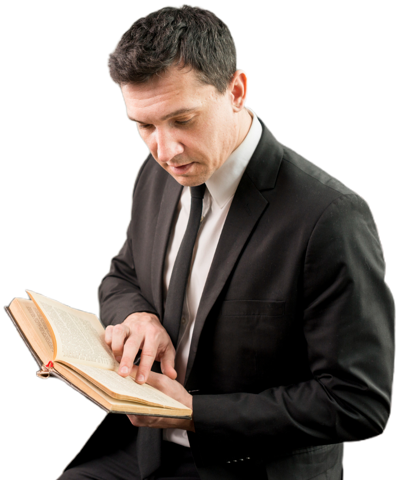 Man in a black suit reading a book, focused expression.