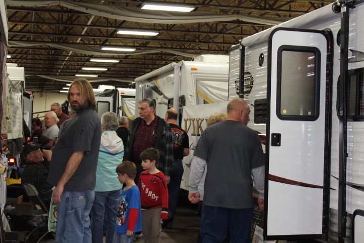 A group of people are standing in a warehouse looking at rvs.