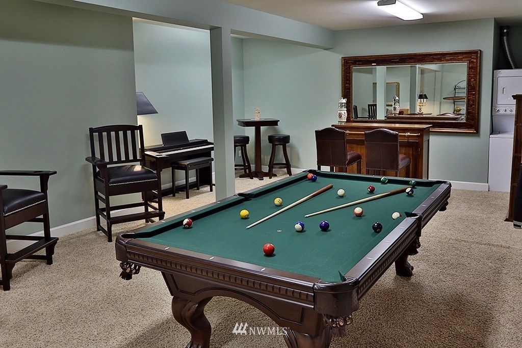 A pool table in a basement with a bar and chairs