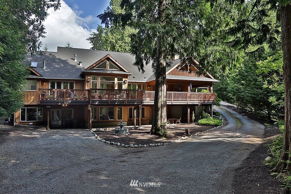 A large house is surrounded by trees and a gravel driveway.