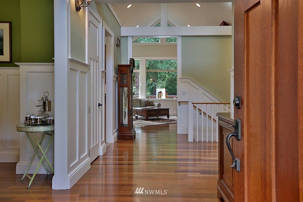 A hallway with a wooden floor and a wooden door leading to a living room and stairs.