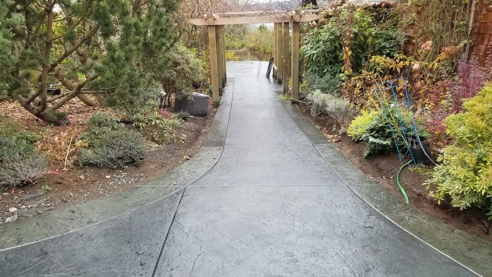 A concrete walkway leading to a wooden archway in a garden.