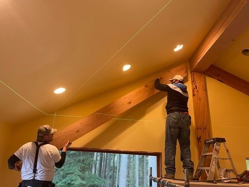 Two men are working on a wooden beam in a room.