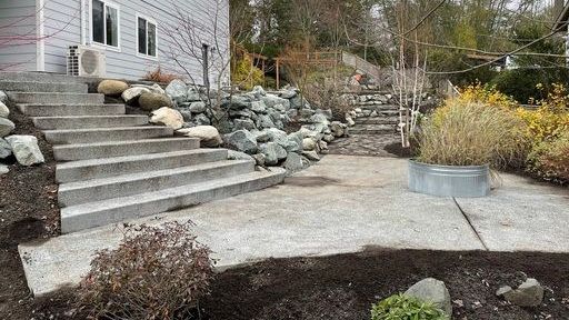 A concrete walkway leading up to a house with stairs and rocks.