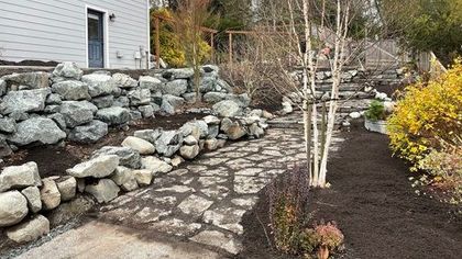 A stone walkway leading to a house surrounded by rocks and trees.