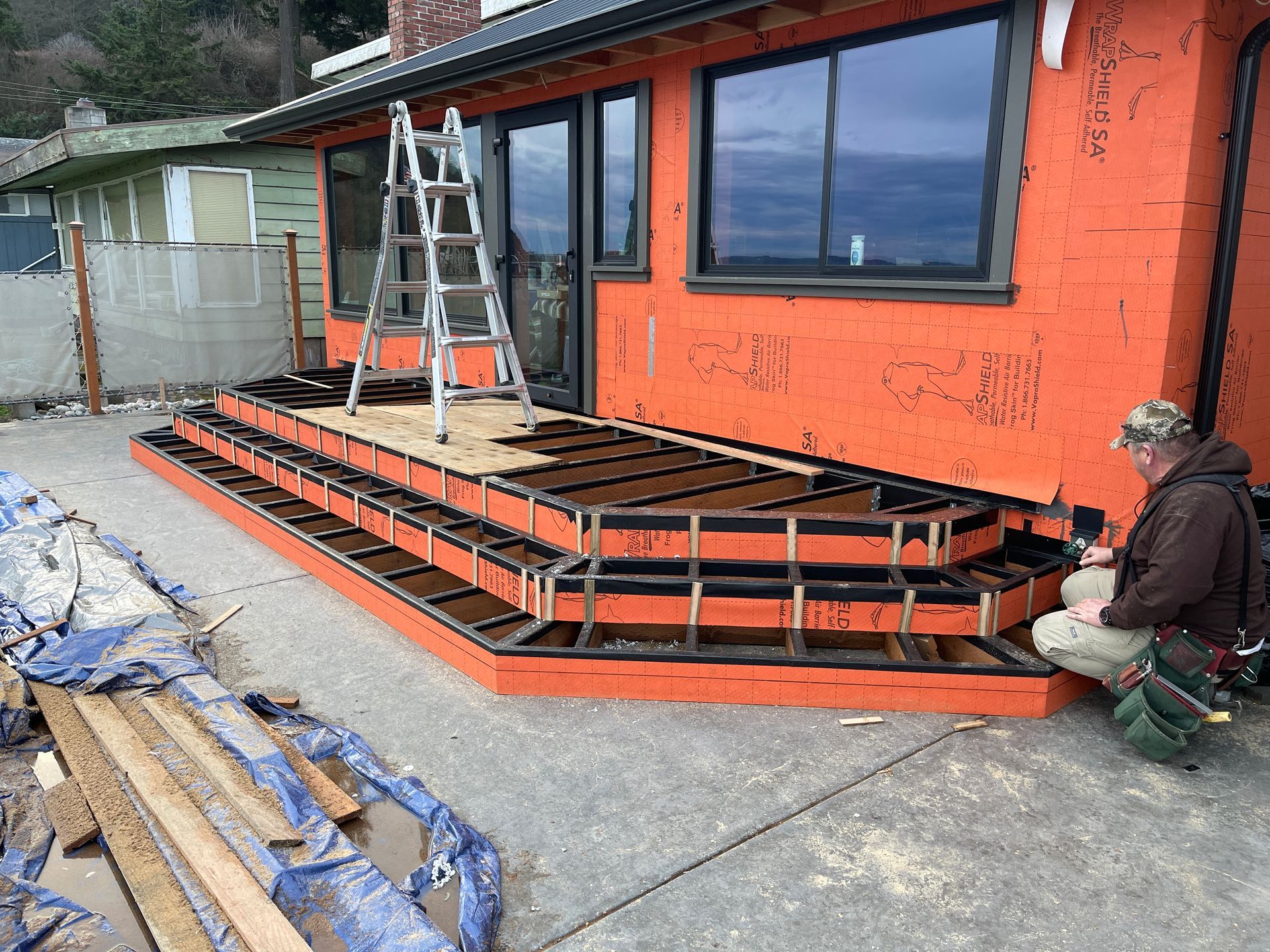 A man is sitting on the sidewalk next to a deck under construction.