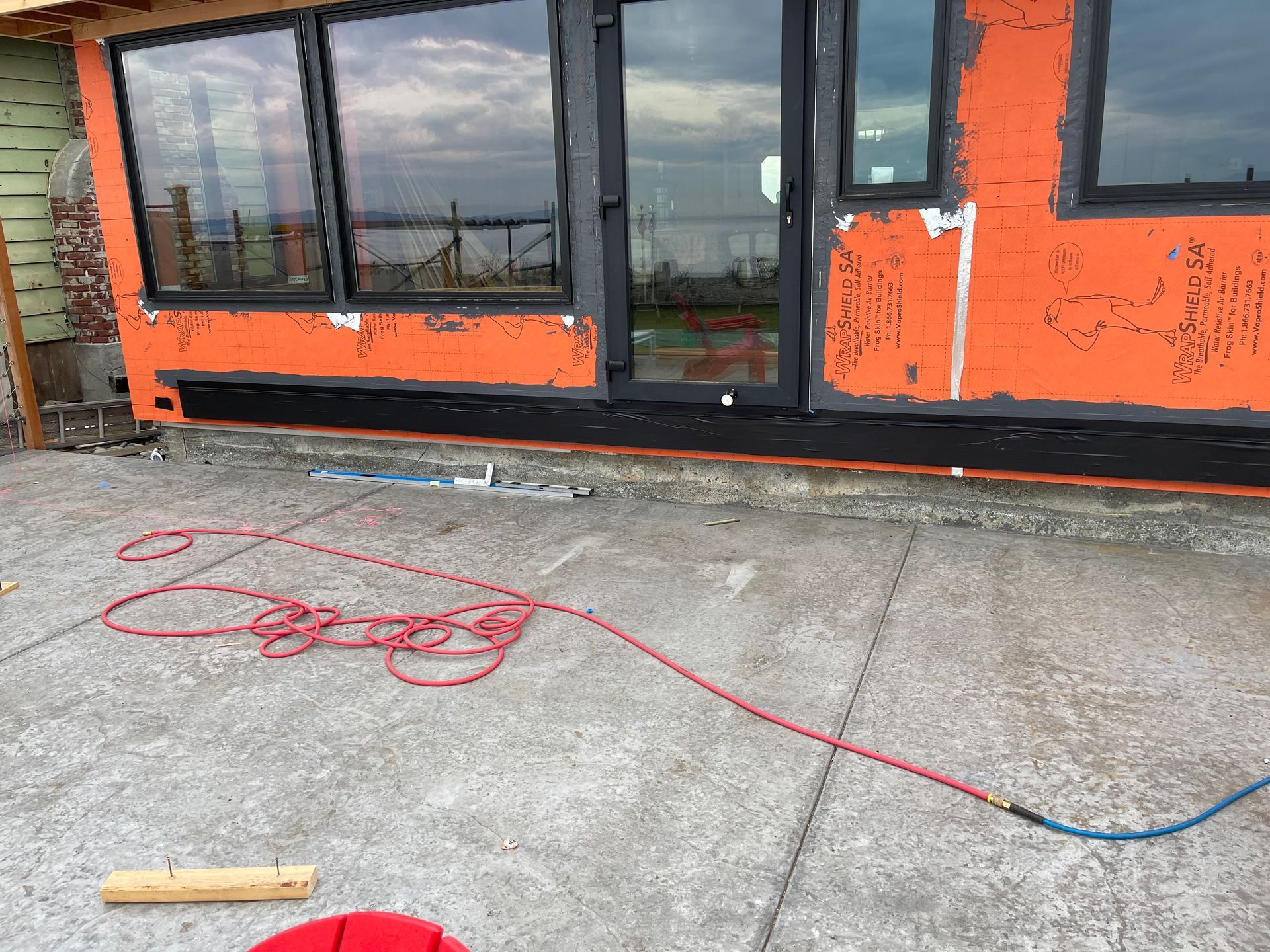 A red cord is laying on the ground in front of a building under construction.