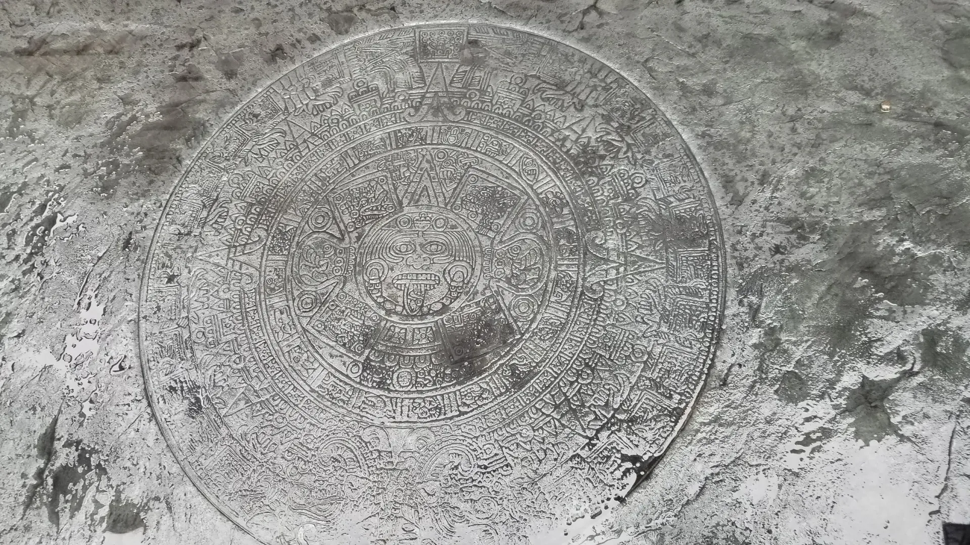 A black and white photo of a manhole cover on a concrete surface.