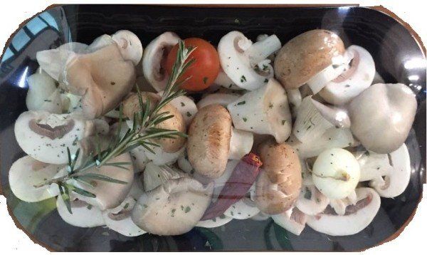 Funghi e pomodori disposti in un vassoio trasparente con un rametto di rosmarino.