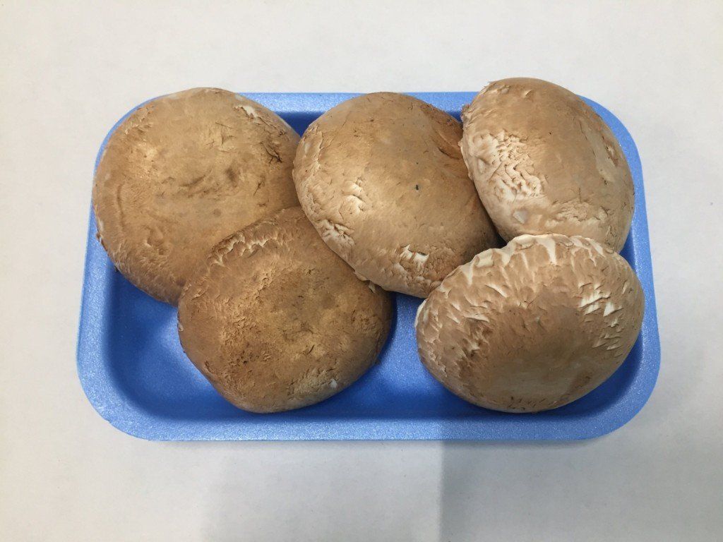 Funghi cremini marroni in un vassoio di polistirolo blu su una superficie bianca.