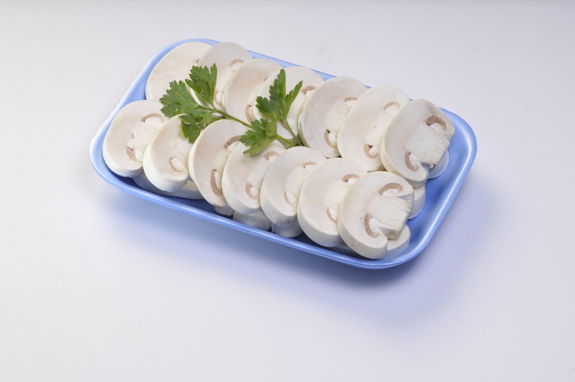 Funghi bianchi affettati, disposti su un vassoio di gommapiuma blu, guarnito con prezzemolo.