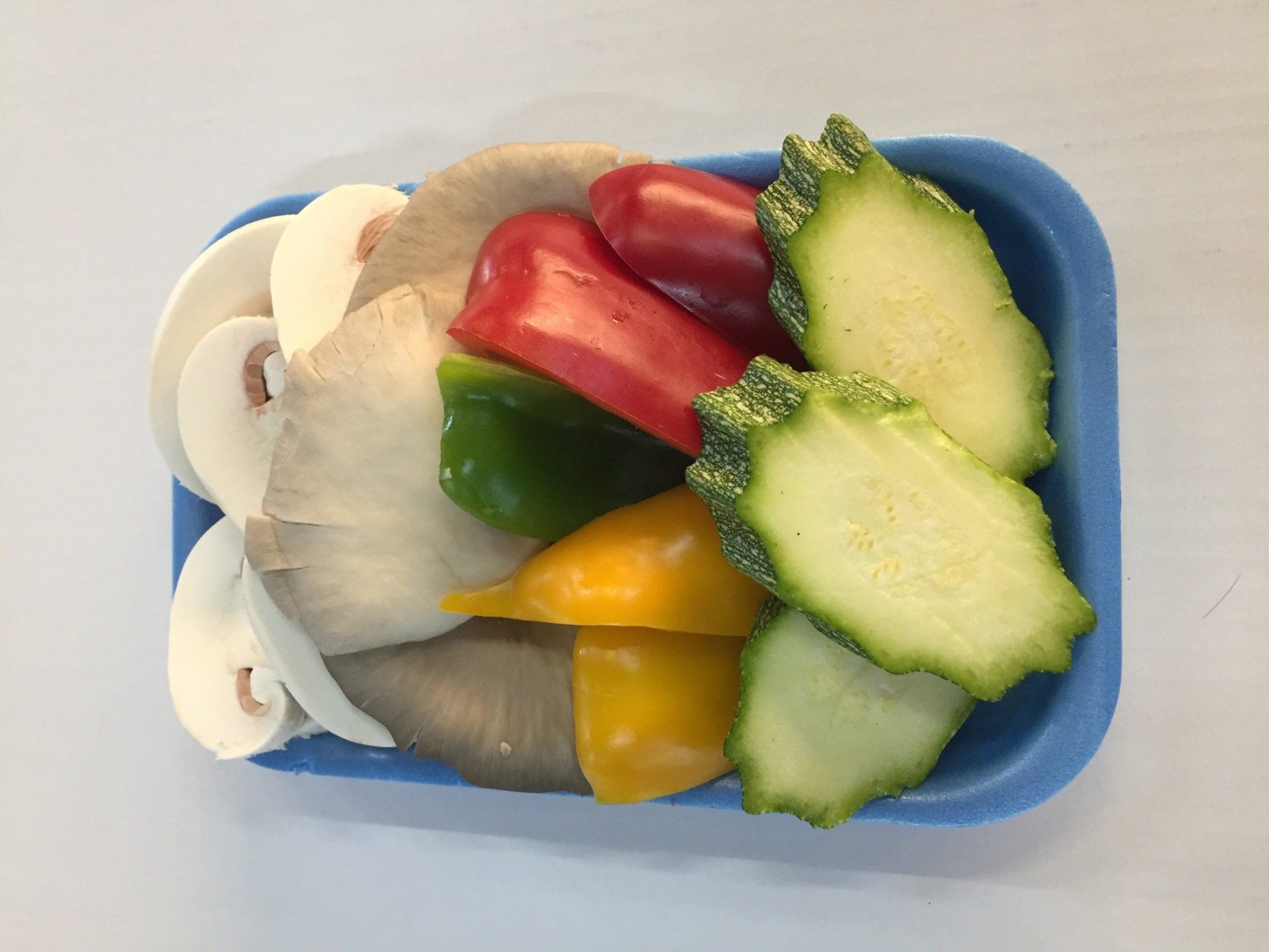 Verdure tagliate a fette: funghi, peperoni (rossi, verdi, gialli) e zucca chayote in un contenitore blu.