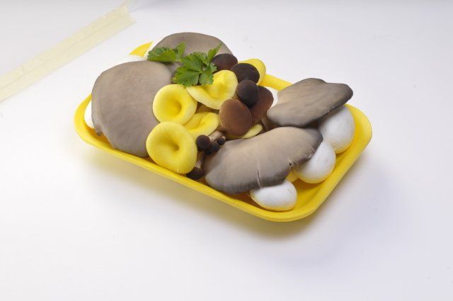 Funghi colorati assortiti su un vassoio di plastica gialla su uno sfondo bianco.