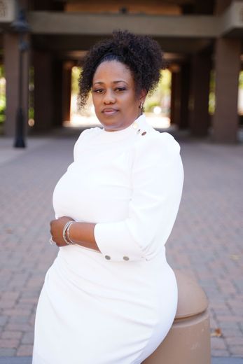 A woman in a white lace top is standing with her arms crossed.