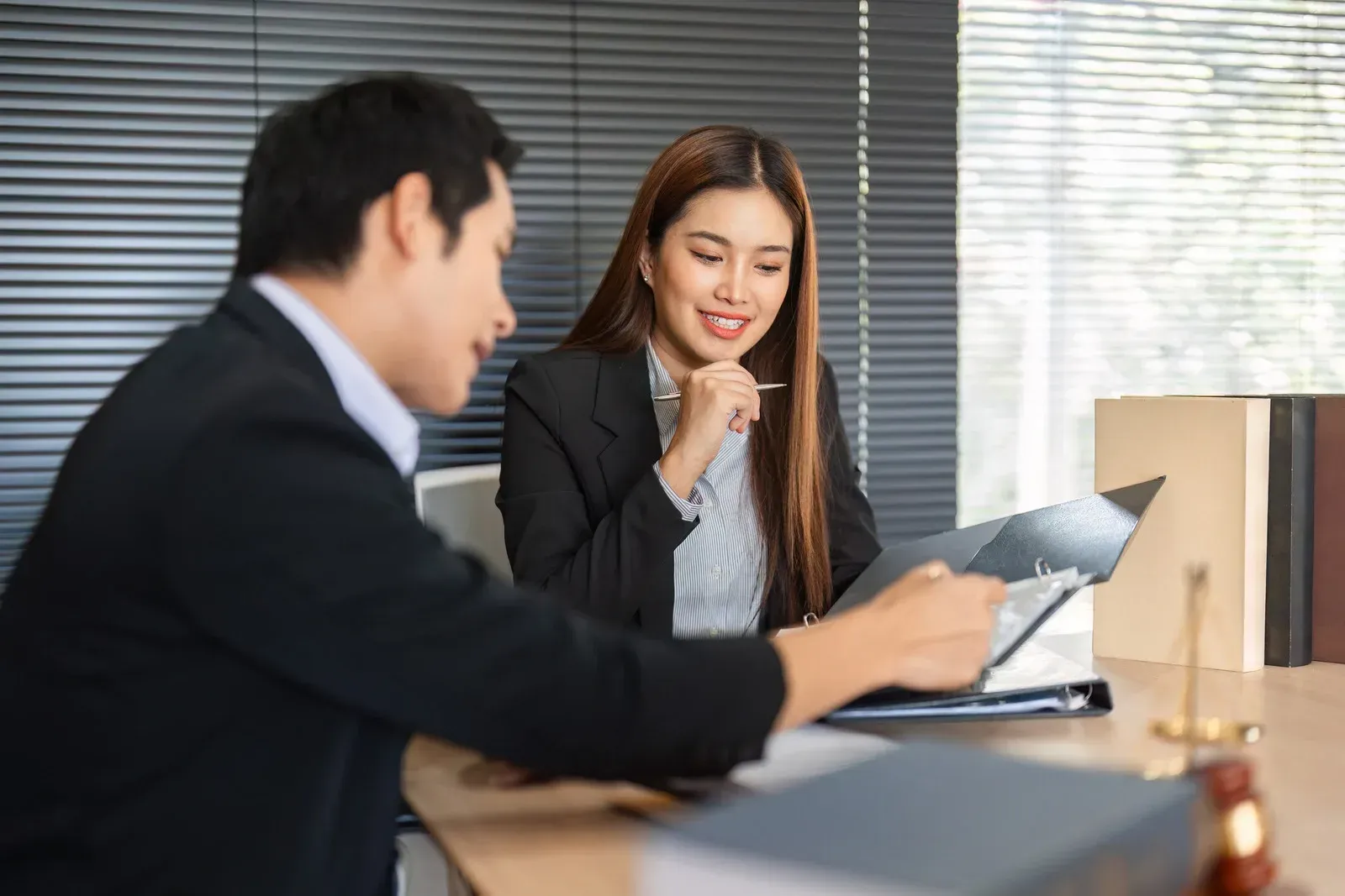 A person in a suit writing in a notebook with a pen, in a library with bookshelves.